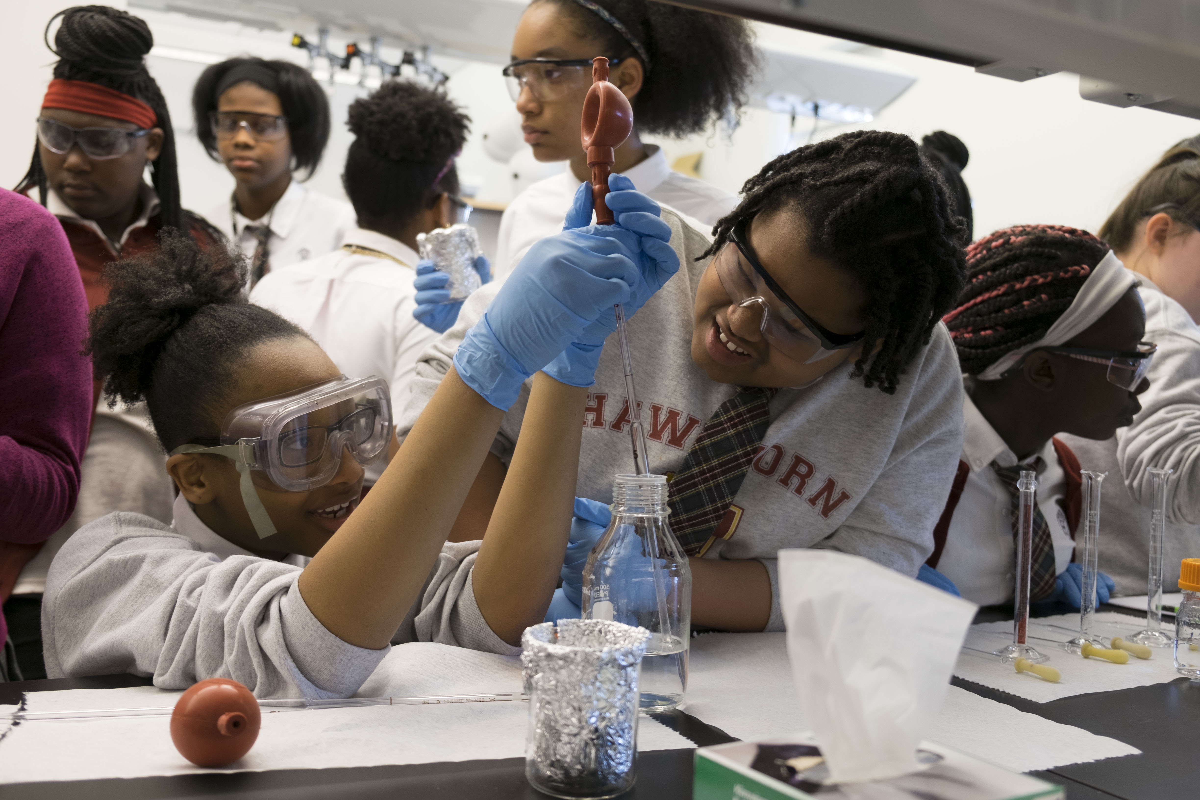 Female African American high school student pipettes a clear liquid while another student watches