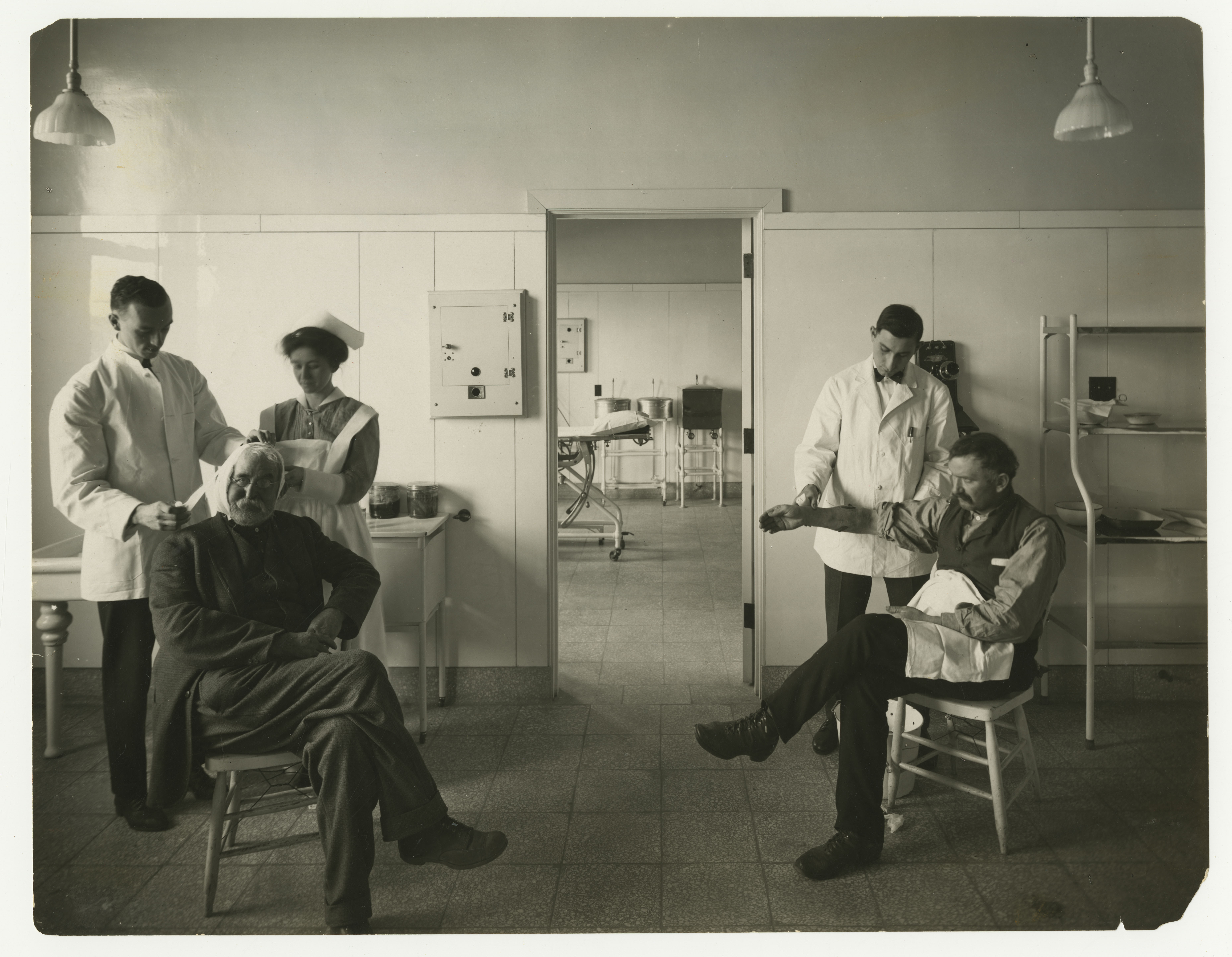 Black and white photo: Three caregivers treat two seated patients