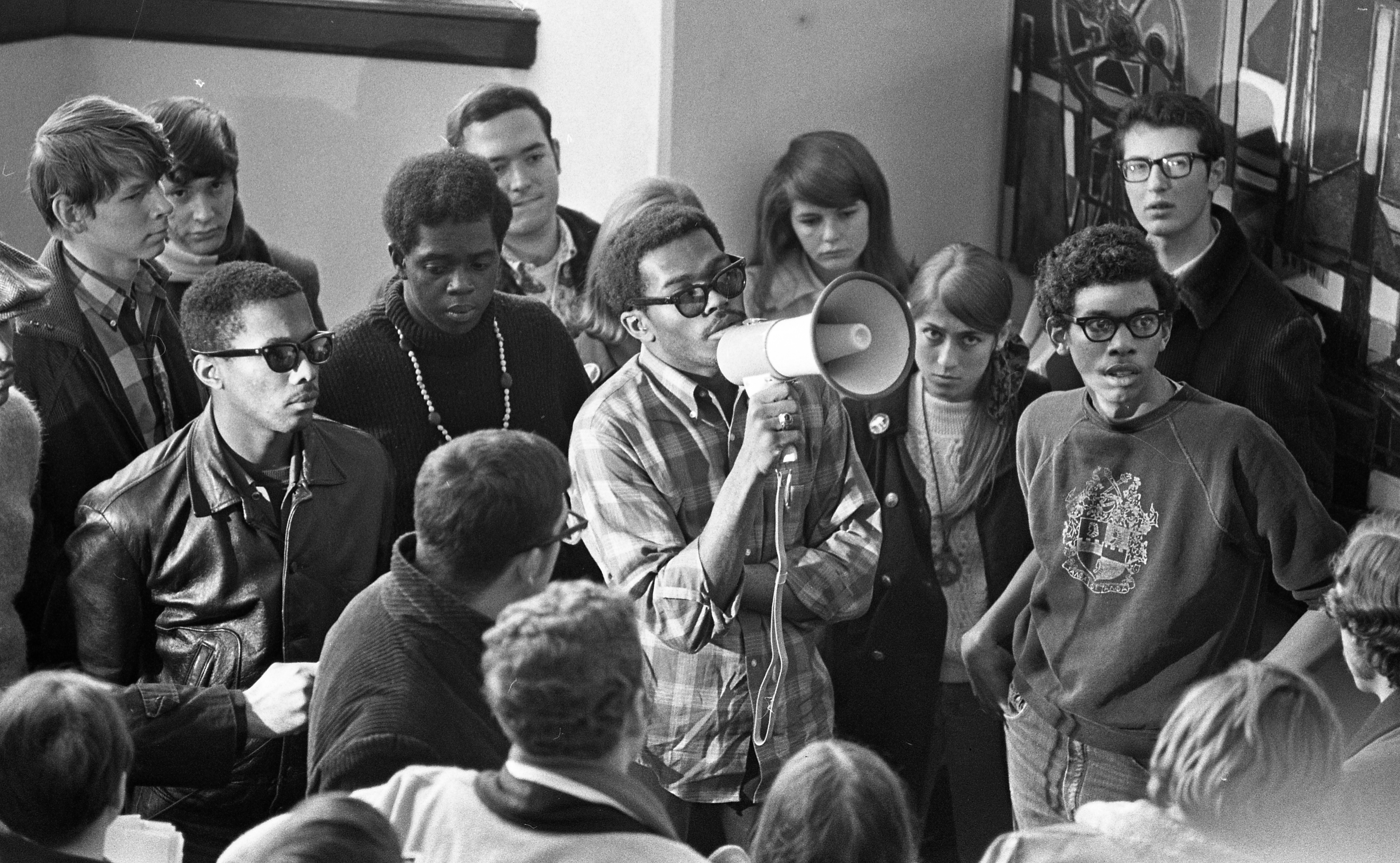 A group of students stands around a black student speaking into a megaphone