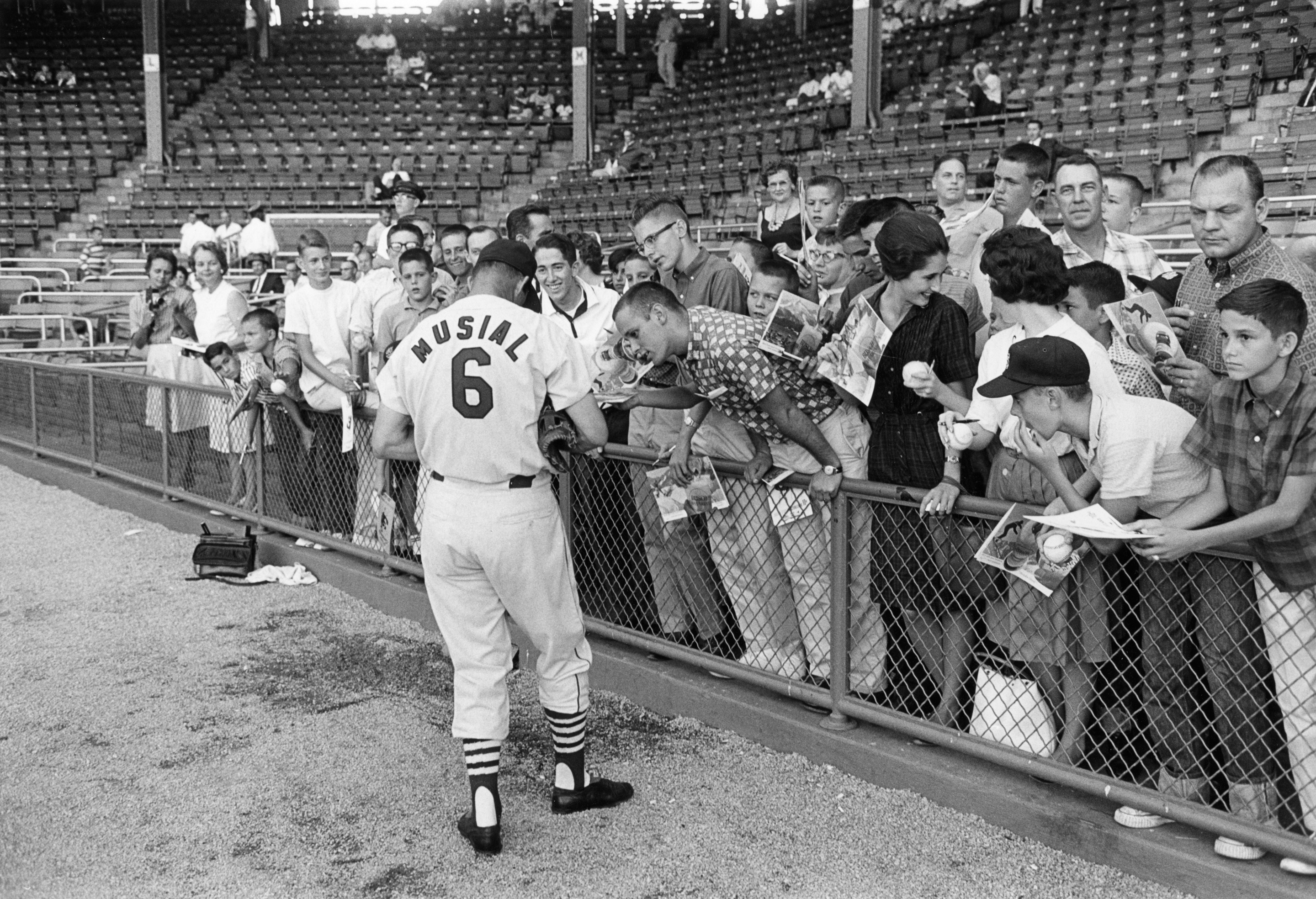 Black and white photo of Stan Musial signing autographs for crowd of spectators in a stadium