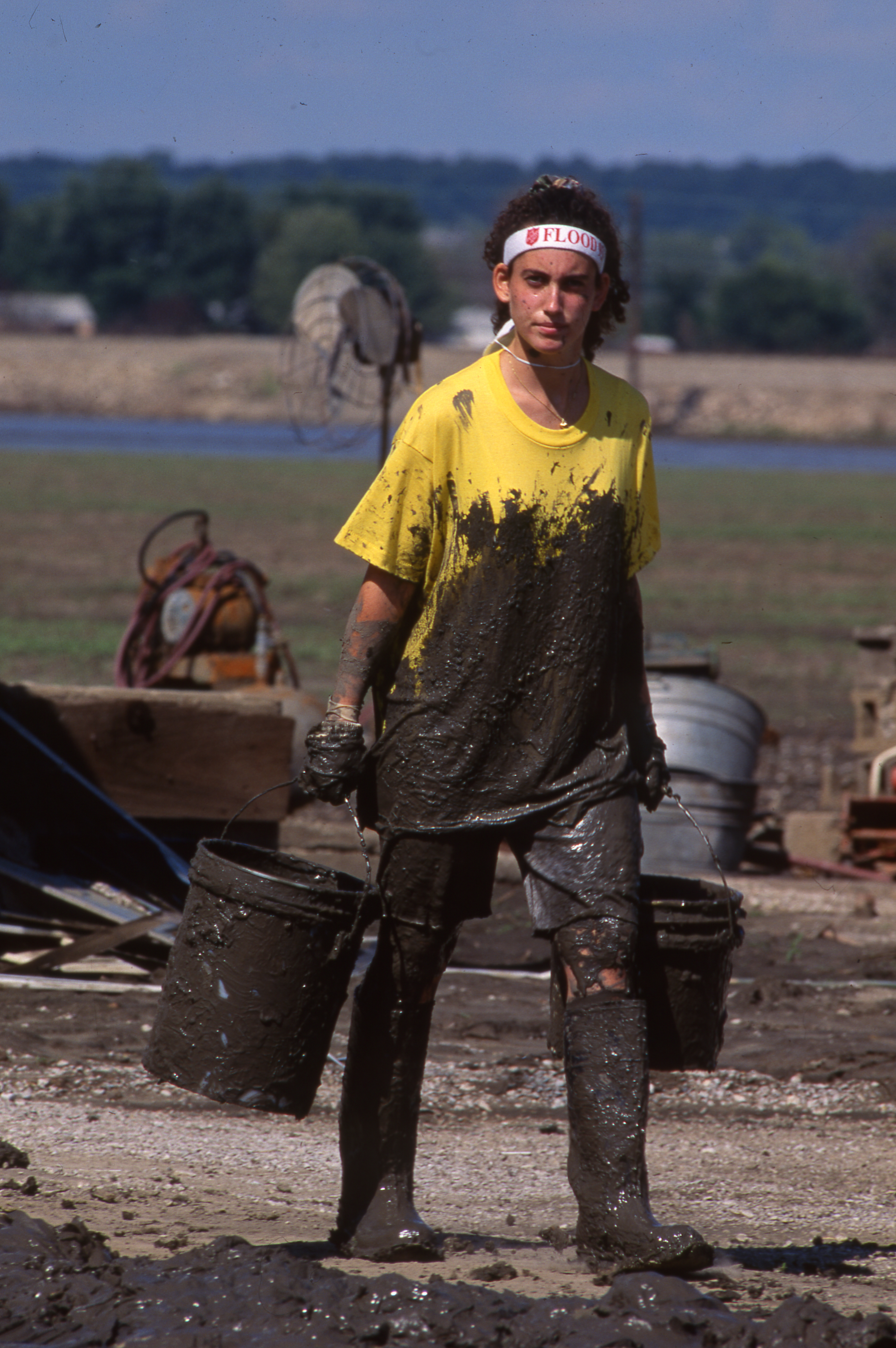 Student in yellow shirt covered in mud carrying buckets